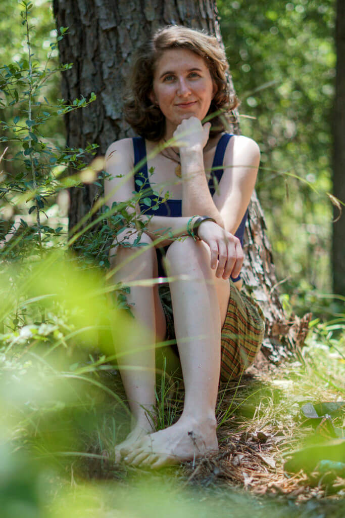 Model wearing navy blue crop tank sitting in forest smiling.