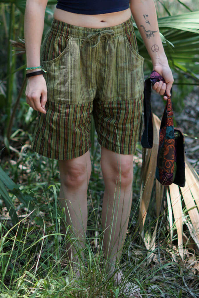 Model wearing navy blue crop tank with striped green hippie shorts standing in forest smiling.