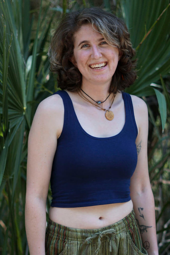 Model wearing navy blue crop tank with striped green shorts standing in forest smiling.