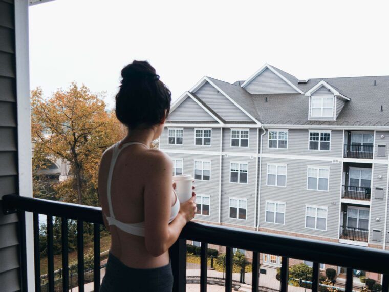 A person with dark hair in a bun stands on a funky balcony, holding a mug, and looks toward a gray apartment building across the way. Soul Flower Blog: Hippie Style & Kind Living
