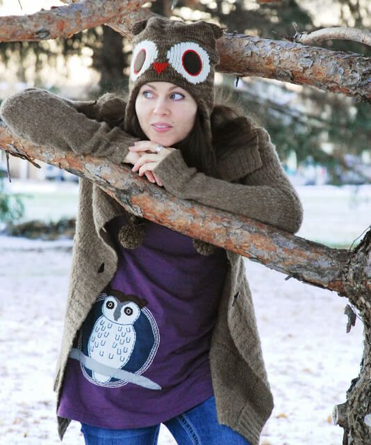 A woman wearing an owl hat and a Woot! Snowy Owl Organic Tunic leans on a tree branch outdoors in a snowy setting. Soul Flower Blog: Hippie Style & Kind Living