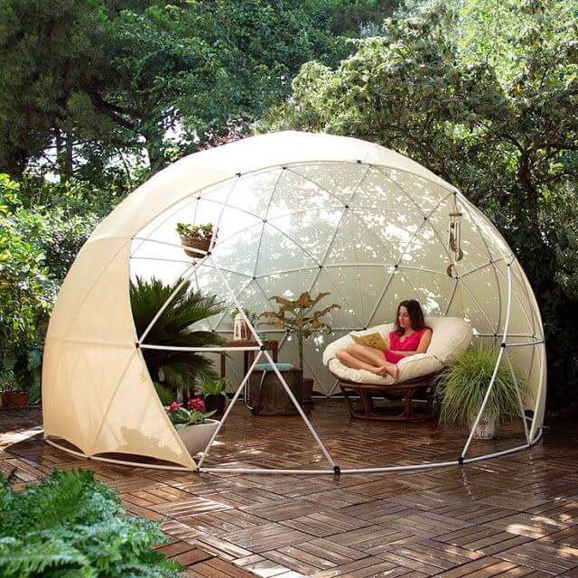 A woman sits and reads on a round chair inside a transparent geodesic dome on a patio surrounded by greenery and potted plants—one of the Top Pins August 2015. Soul Flower Blog: Hippie Style & Kind Living
