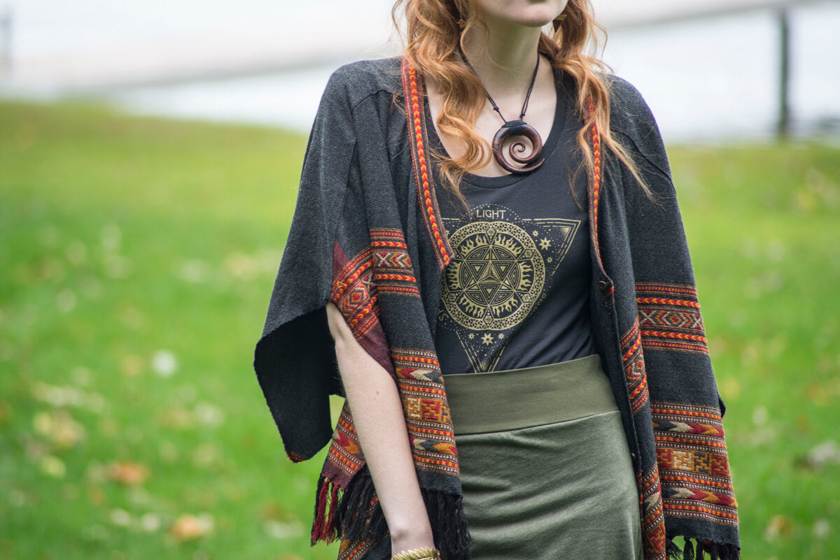 Woman wearing a funky patterned shawl, a boho hippie t-shirt with a geometric design, a green skirt, and a spiral pendant necklace, standing outdoors on a grassy area. Soul Flower Blog: Hippie Style & Kind Living