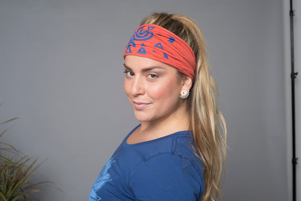Woman with long blonde hair wearing a boho red patterned headband, blue shirt, and sun-shaped earrings poses in front of a neutral gray background. Soul Flower Blog: Hippie Style & Kind Living