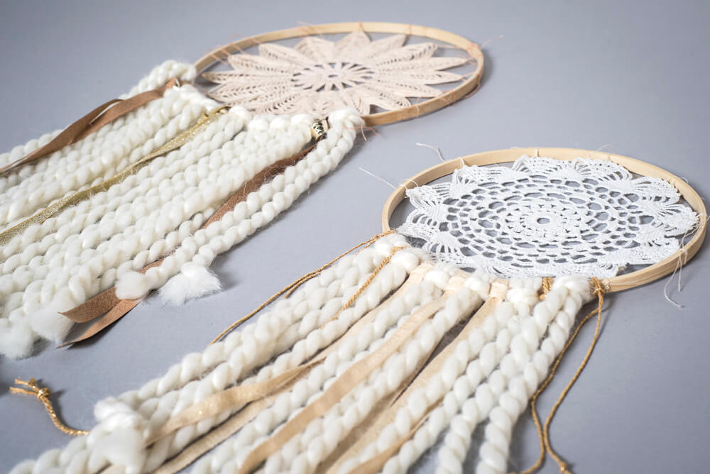 Two handmade boho dreamcatchers with crochet centers, decorated with white yarn, ribbons, and lace, lying on a grey surface. Soul Flower Blog: Hippie Style & Kind Living