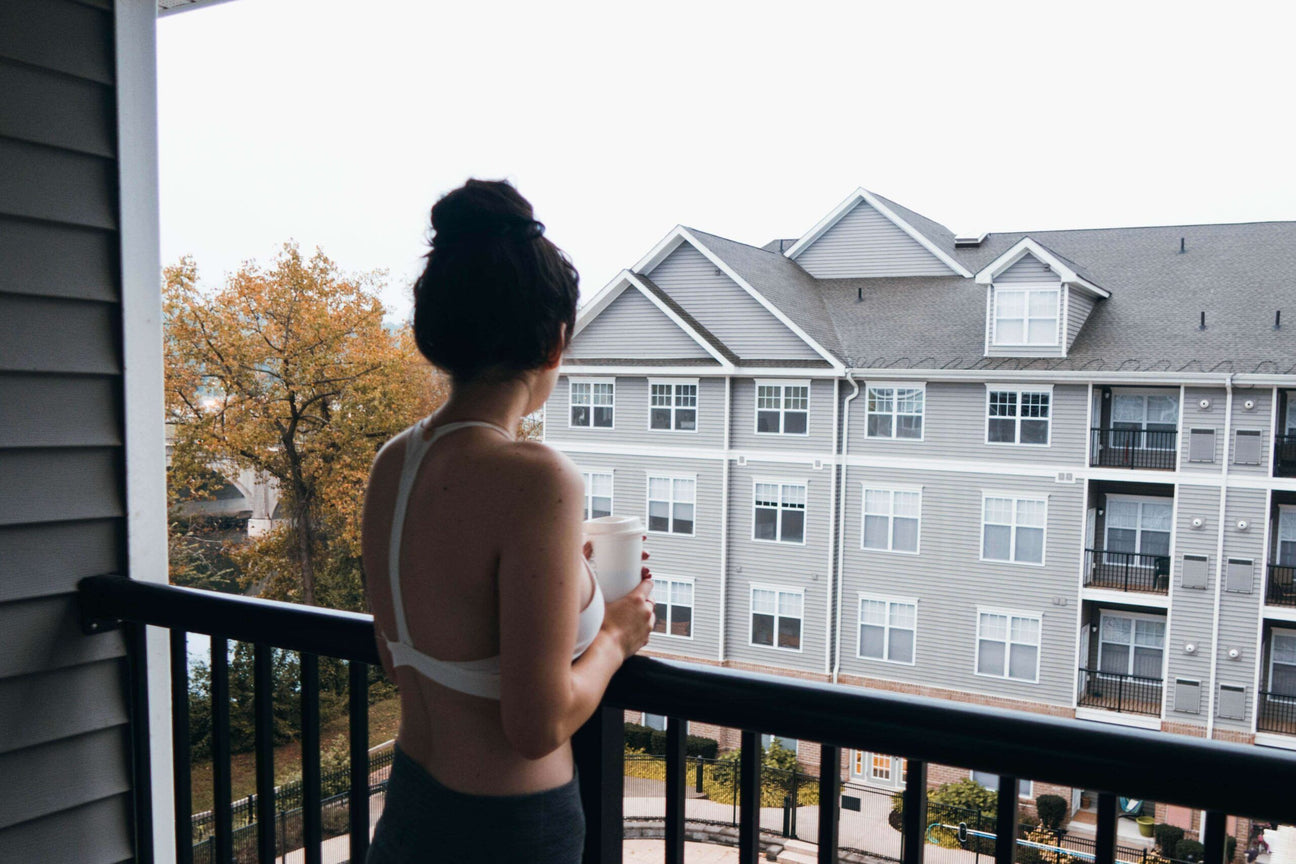 A person with dark hair in a bun stands on a funky balcony, holding a mug, and looks toward a gray apartment building across the way. Soul Flower Blog: Hippie Style & Kind Living