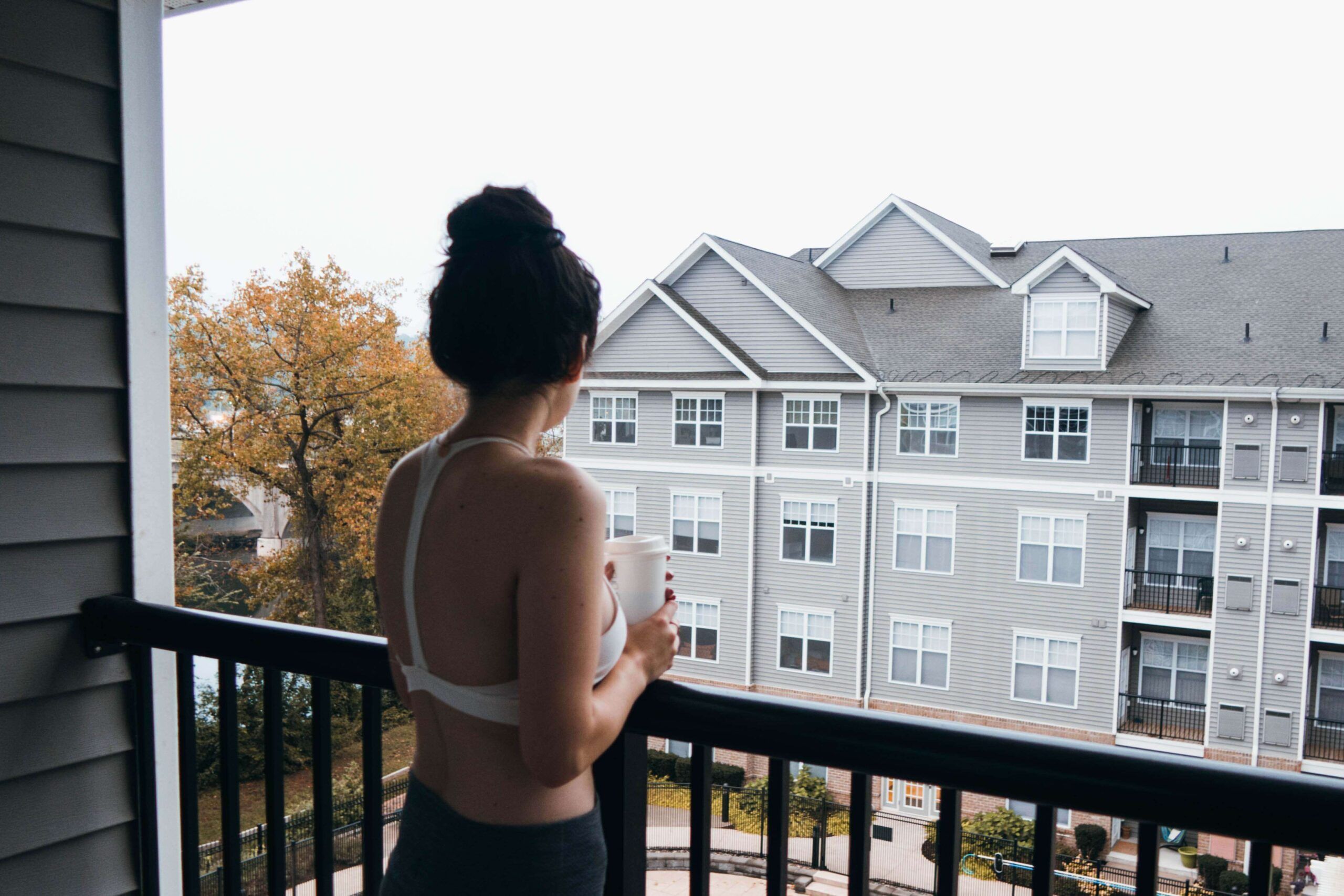 A person with dark hair in a bun stands on a funky balcony, holding a mug, and looks toward a gray apartment building across the way. Soul Flower Blog: Hippie Style & Kind Living