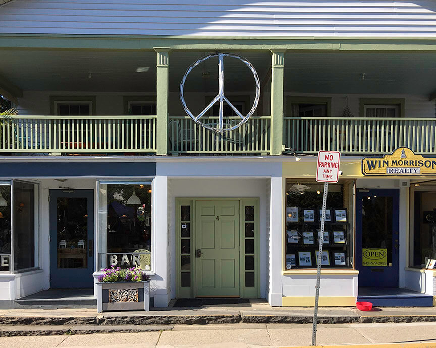 Two-story boho building with a large peace symbol above a green door, flanked by a funky bar and realty office; a No Parking Any Time sign stands on the sidewalk. Soul Flower Blog: Hippie Style & Kind Living