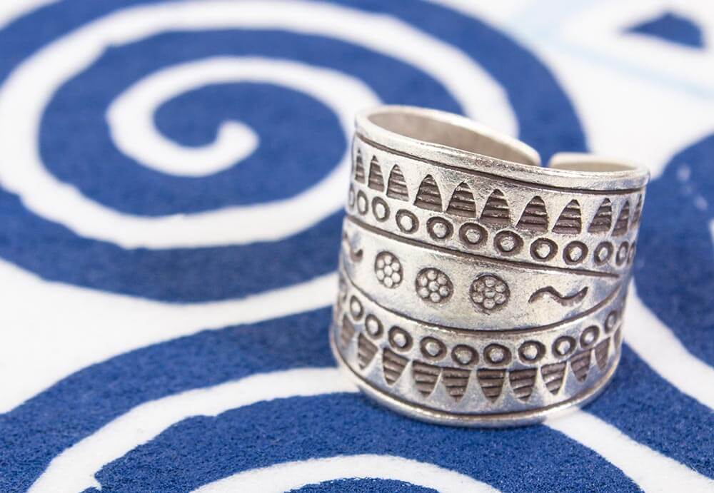 A wide silver ring with geometric and dotted engraved patterns rests on a surface with bold blue spiral designs, echoing a natural style perfect for mindful living. Soul Flower Blog: Hippie Style & Kind Living