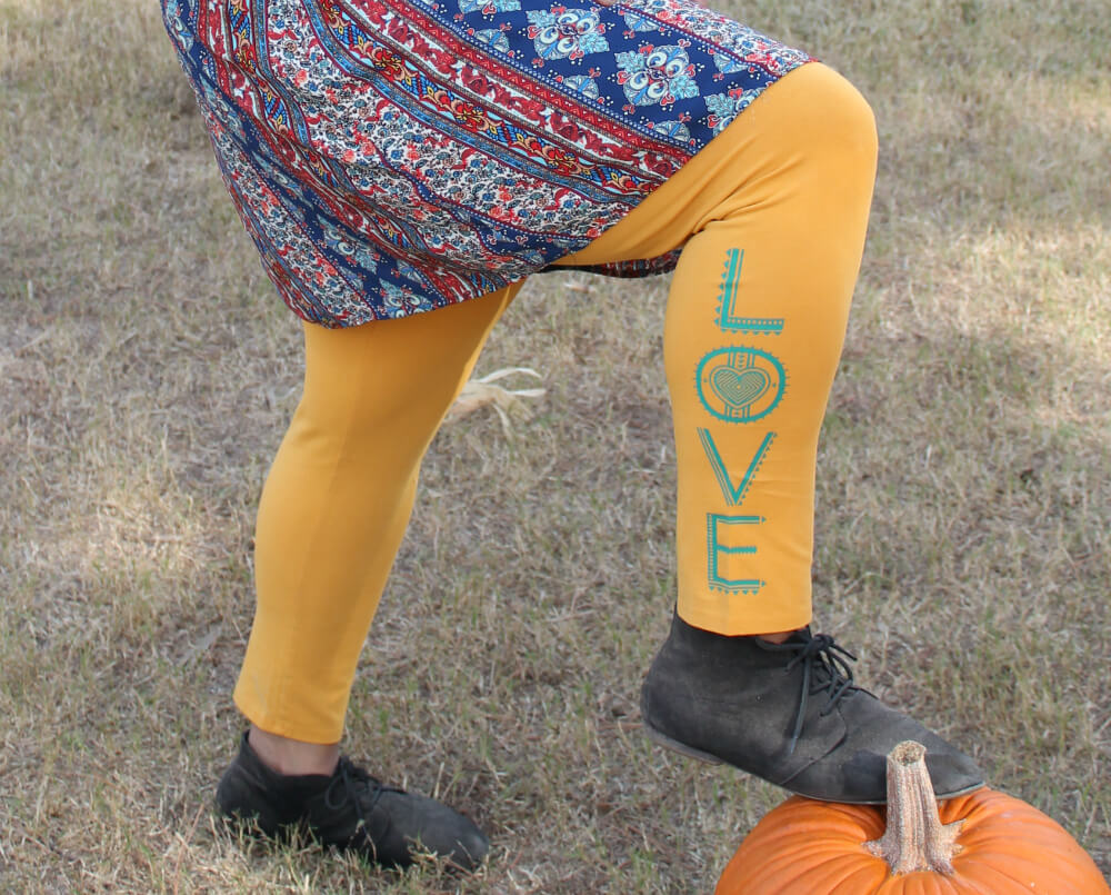 Person in yellow leggings with LOVE written on one leg, wearing black shoes and a funky hippie t-shirt, stands outdoors with foot resting on a pumpkin. Soul Flower Blog: Hippie Style & Kind Living