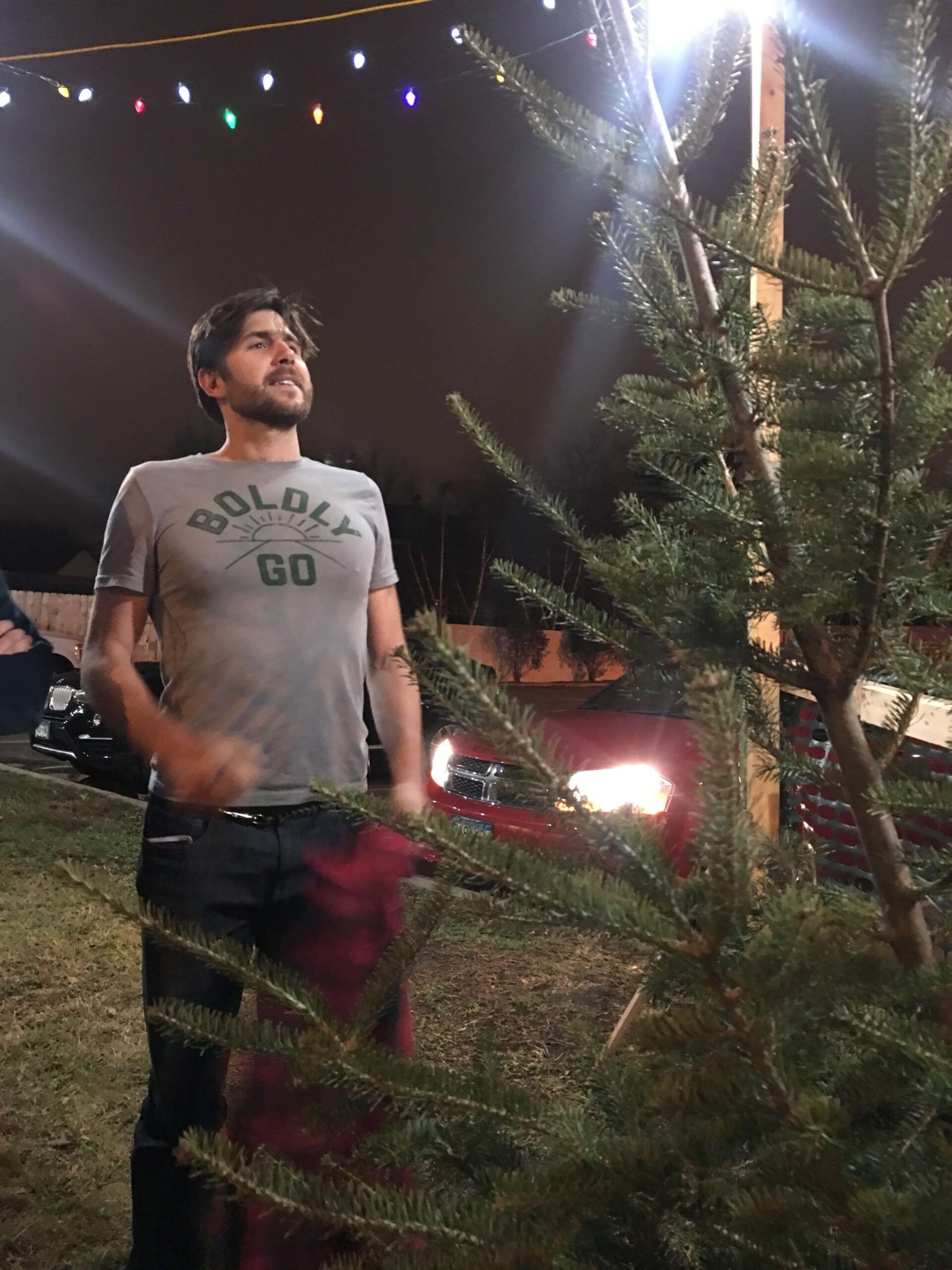 A man stands outdoors at night near a boho-inspired Christmas tree under string lights, with parked cars and another person visible in the background. Soul Flower Blog: Hippie Style & Kind Living