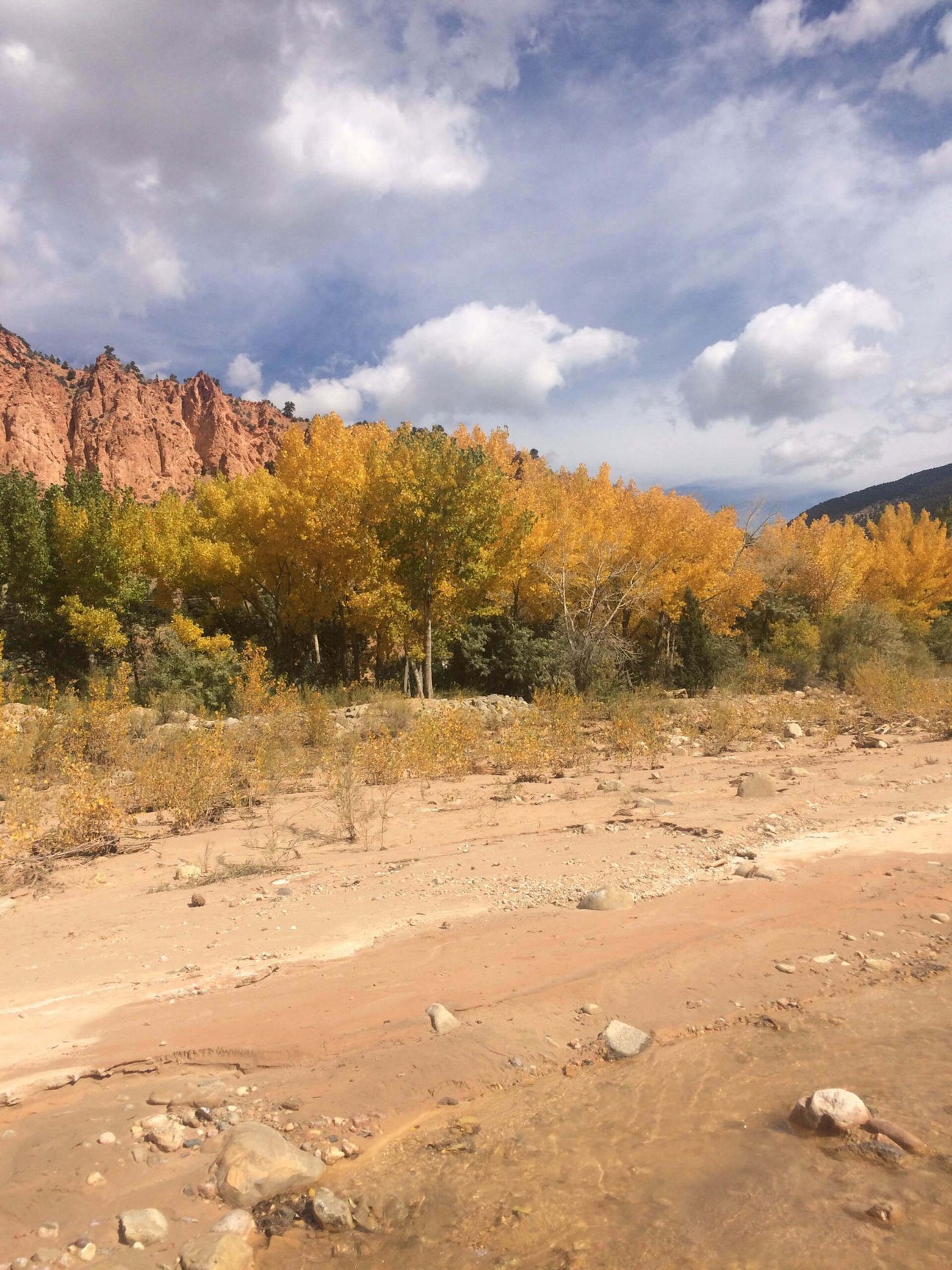 A sandy, rocky stream bed in the foreground with yellow-leaved trees and earthy red cliffs in the background under a partly cloudy sky. Soul Flower Blog: Hippie Style & Kind Living