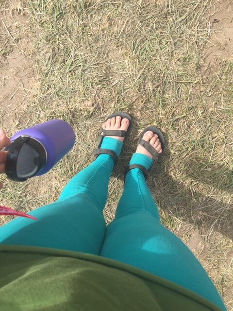 Person wearing teal leggings and sandals stands on dry grass, holding a purple water bottle. Soul Flower Blog: Hippie Style & Kind Living