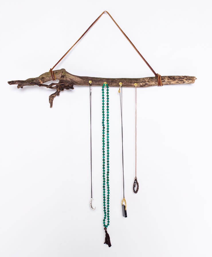 A driftwood branch is hung on the wall with a leather strap, serving as a boho jewelry holder with several necklaces hanging from attached hooks. Soul Flower Blog: Hippie Style & Kind Living