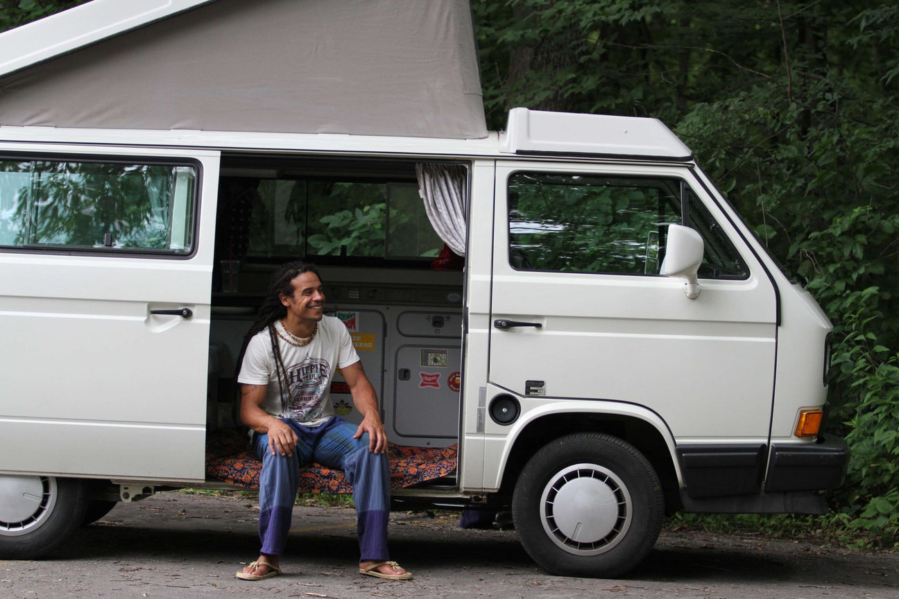 A person sits in the doorway of a white camper van parked on a road, surrounded by trees and greenery. Soul Flower Blog: Hippie Style & Kind Living