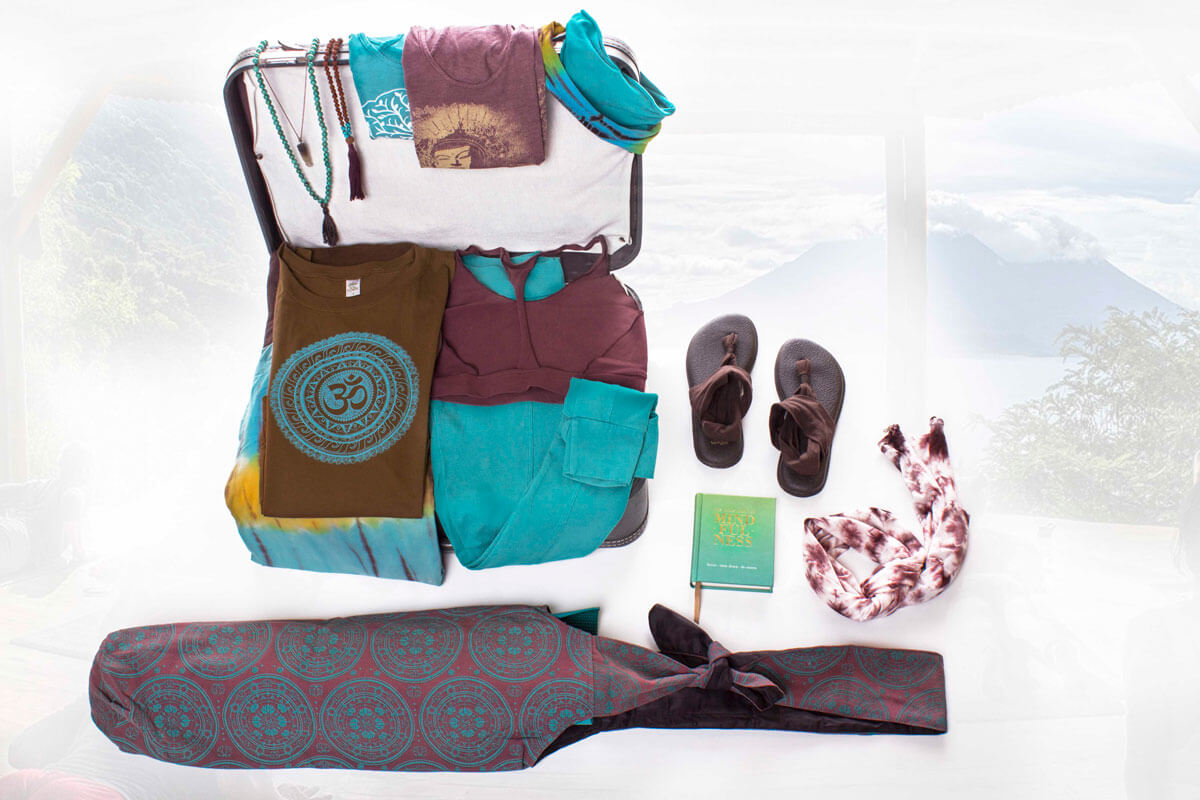 A flat lay of yoga travel essentials, including clothes, sandals, a yoga mat bag, a book, jewelry, and a tie-dye scarf—perfect inspiration for your next adventure or to help you ace your Travel Style Quiz. Soul Flower Blog: Hippie Style & Kind Living