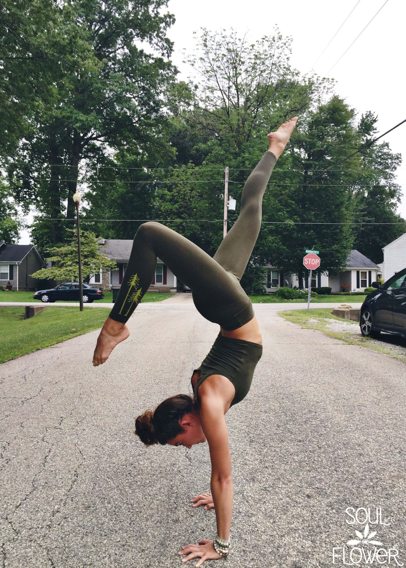 A person in olive green activewear performs a handstand split on a residential street lined with trees and houses. Soul Flower is written in the bottom right corner—Win the Two Pines Leggings!. Soul Flower Blog: Hippie Style & Kind Living