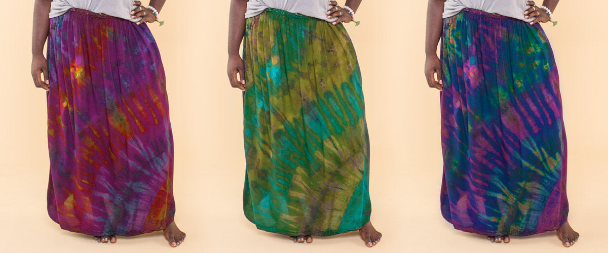Three women stand side by side, each in a long, boho tie-dye skirt—purple-red, green-blue, and blue-purple—showcasing their eco style with feet partially visible. Soul Flower Blog: Hippie Style & Kind Living