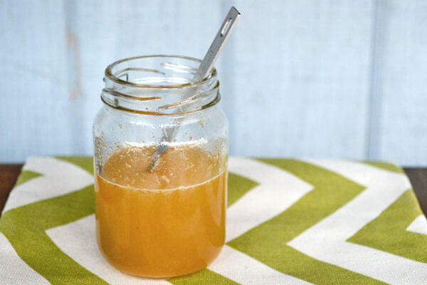 A glass jar containing a cloudy yellow liquid, inspired by the 5 Elixirs to Keep You Healthy This Winter, with a metal spoon inside, placed on a green and white chevron-patterned cloth. Soul Flower Blog: Hippie Style & Kind Living