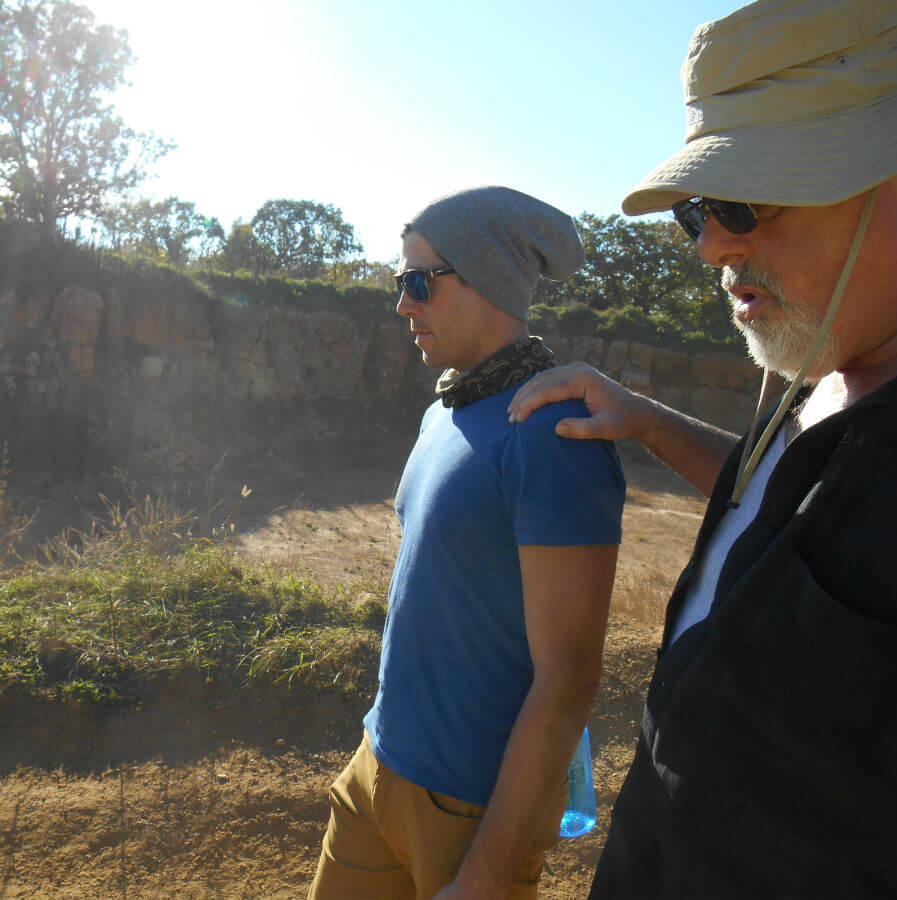 Two men walk outdoors on a sunny day, embracing an earthy vibe—one in a beanie and sunglasses, the other in a hat and sunglasses with a hand on the other's shoulder. Soul Flower Blog: Hippie Style & Kind Living