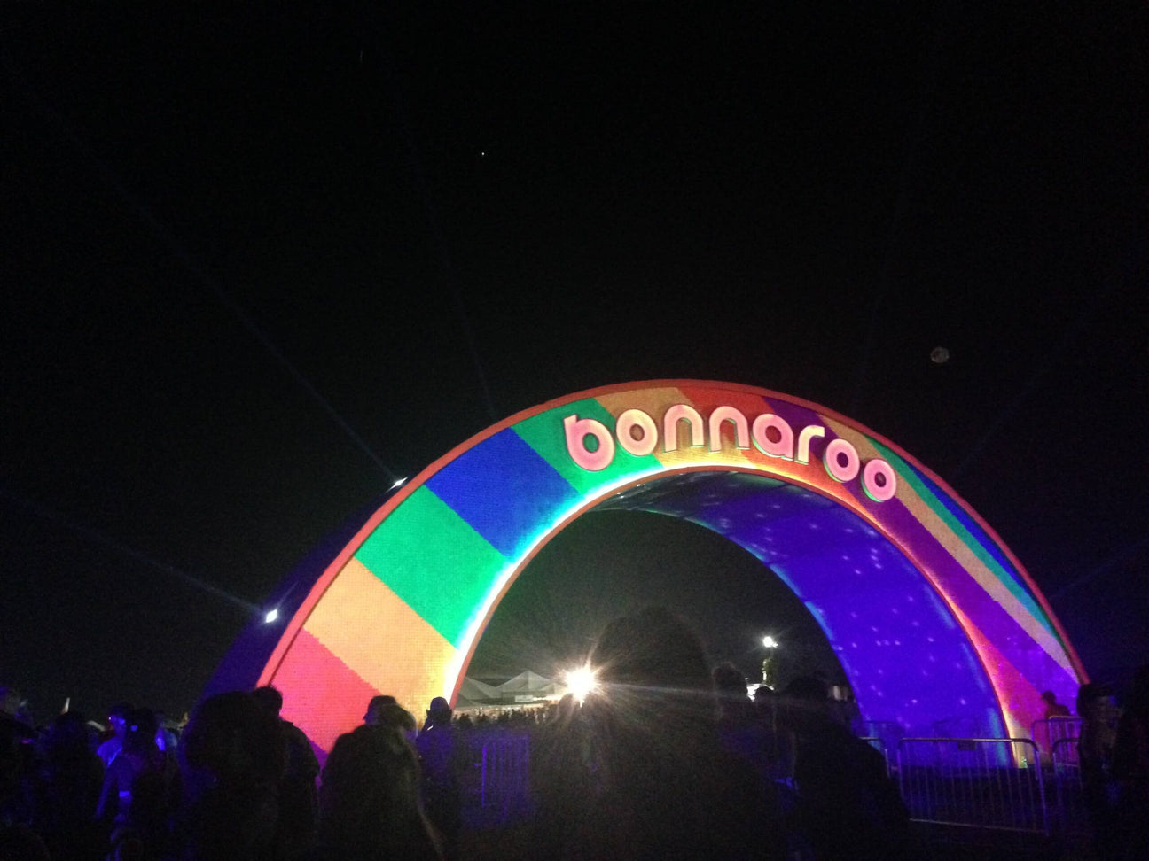 A large, colorful archway with "Bonnaroo - Back to My Roots" illuminated at night, as people gather underneath and spotlights shine in the background. Soul Flower Blog: Hippie Style & Kind Living