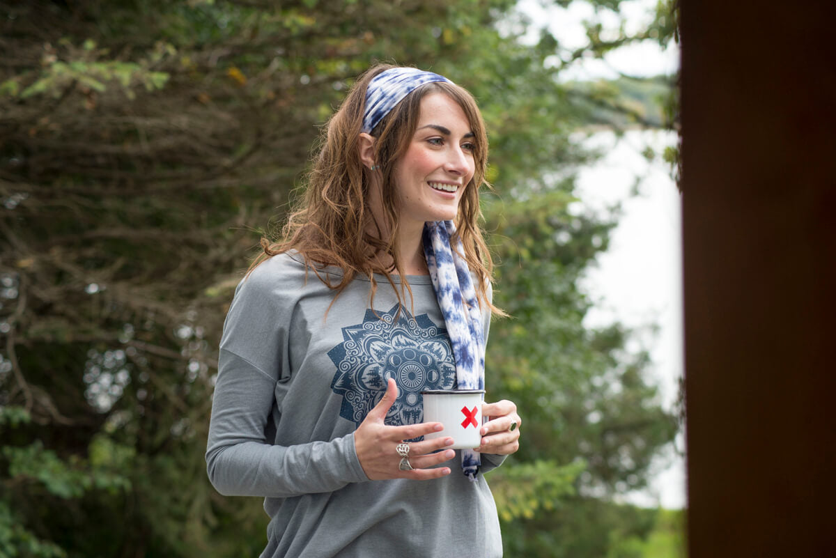 A woman with long hair and a funky patterned headband holds a white mug with a red X, standing outdoors near trees and smiling. Soul Flower Blog: Hippie Style & Kind Living