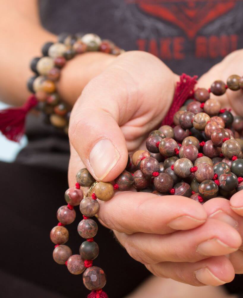 Close-up of hands holding a string of brown and red prayer beads with red tassels, perfect for those choosing mala beads for meditation or spiritual focus. Soul Flower Blog: Hippie Style & Kind Living