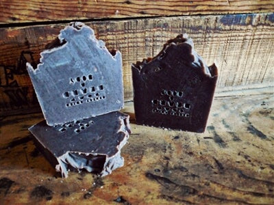 Two dark, jagged-edge bars of soap with imprinted text sit on a worn wooden surface, bringing an earthy touch to the rustic wood backdrop. Soul Flower Blog: Hippie Style & Kind Living