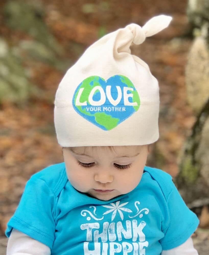 Baby wearing a natural white hat with a blue and green heart reading LOVE YOUR MOTHER and a blue shirt that says THINK HIPPIE, looking down. Soul Flower Blog: Hippie Style & Kind Living
