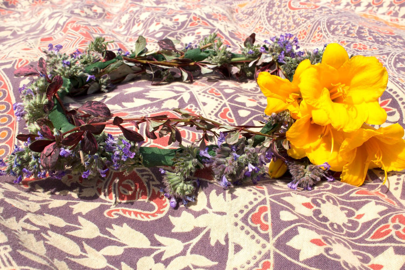A Hippie Flower Crown made of yellow flowers, purple blossoms, and greenery lies on a patterned fabric background. Soul Flower Blog: Hippie Style & Kind Living