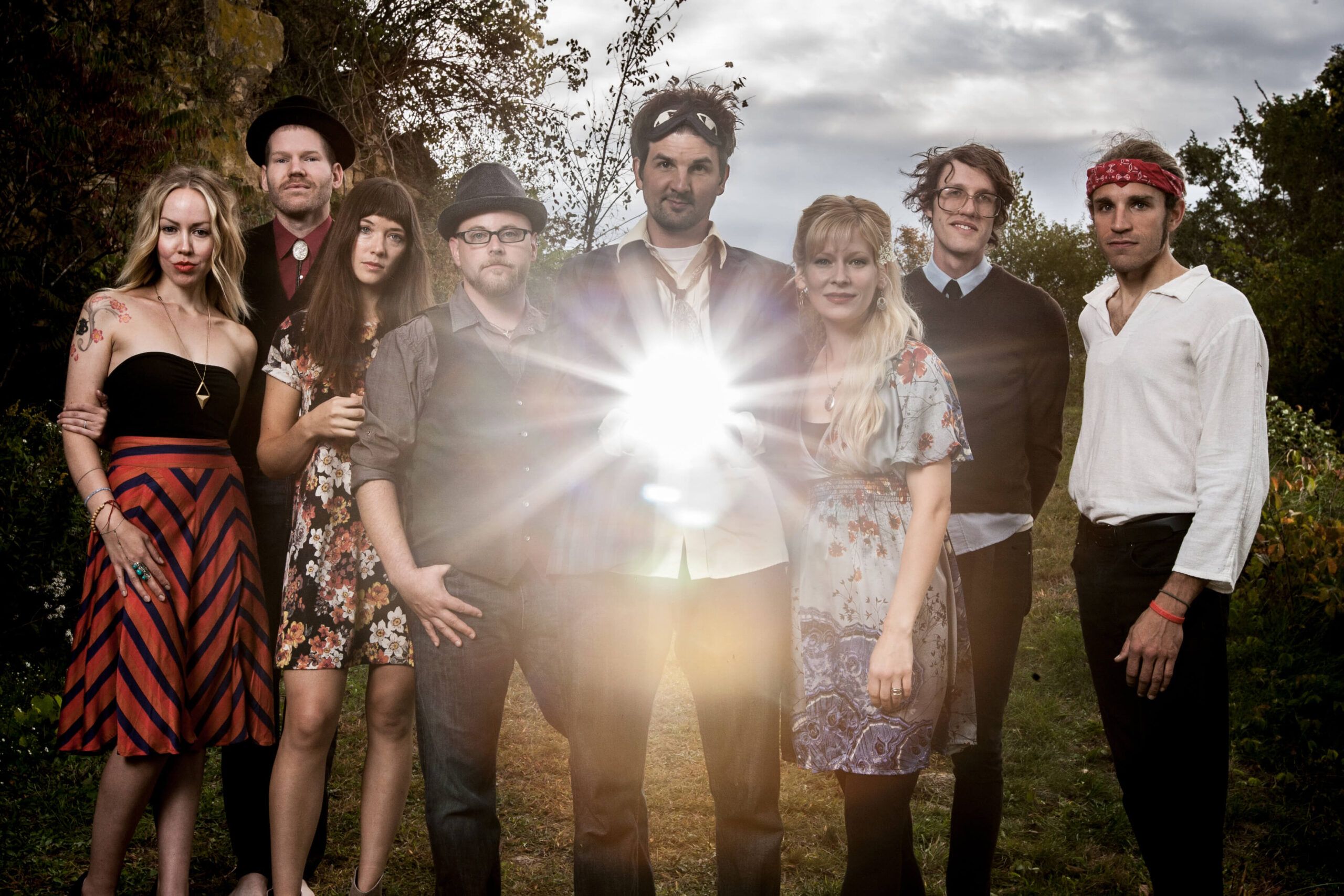 Eight adults stand outdoors in a line, facing the camera. The person in the center holds a bright, glowing light that obscures their hands, adding a touch of boho charm to this natural gathering. Soul Flower Blog: Hippie Style & Kind Living