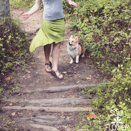 Person in a grey top and green skirt walks on a forest path with a small brown and white dog nearby. The phrase "My Thoughts are Clouds..." drifts above, with the Soul Flower logo in the lower right corner. Soul Flower Blog: Hippie Style & Kind Living