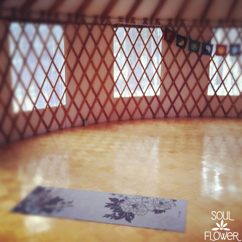 A single yoga mat is placed on a wooden floor inside a yurt with lattice walls, as colorful flags sway in the background—a peaceful space where all I could do was breathe. Soul Flower Blog: Hippie Style & Kind Living