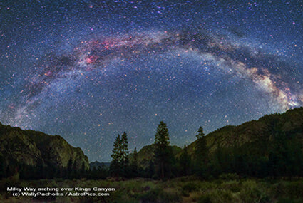 The Milky Way galaxy arches brightly over a dark, eco-inspired, tree-filled valley in Kings Canyon at night. Dense stars illuminate the earthy landscape above forested mountains. Soul Flower Blog: Hippie Style & Kind