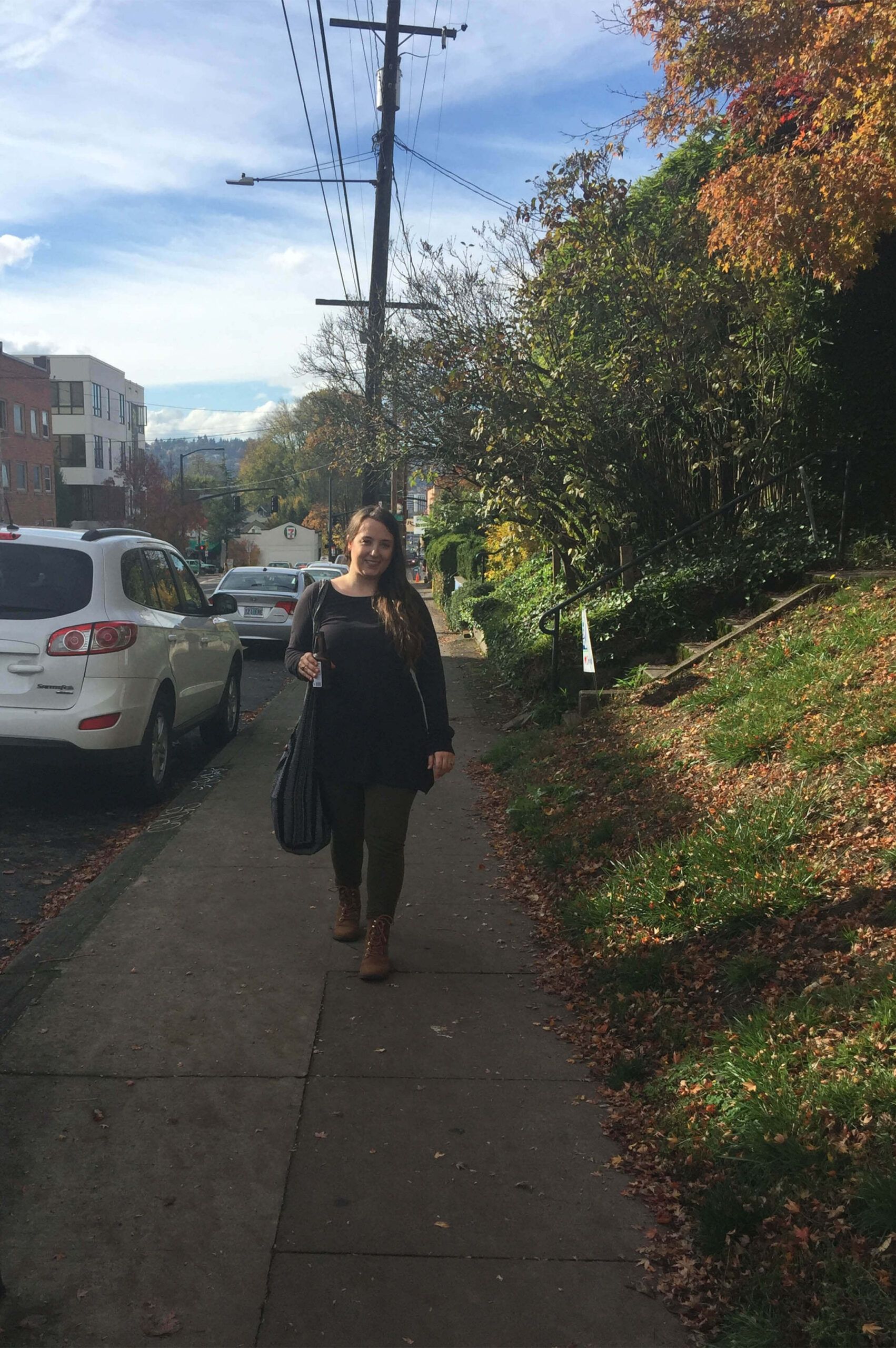 A woman with an eco boho vibe walks on a sidewalk beside parked cars and a grassy hill with autumn trees under a partly cloudy sky. Soul Flower Blog: Hippie Style & Kind Living