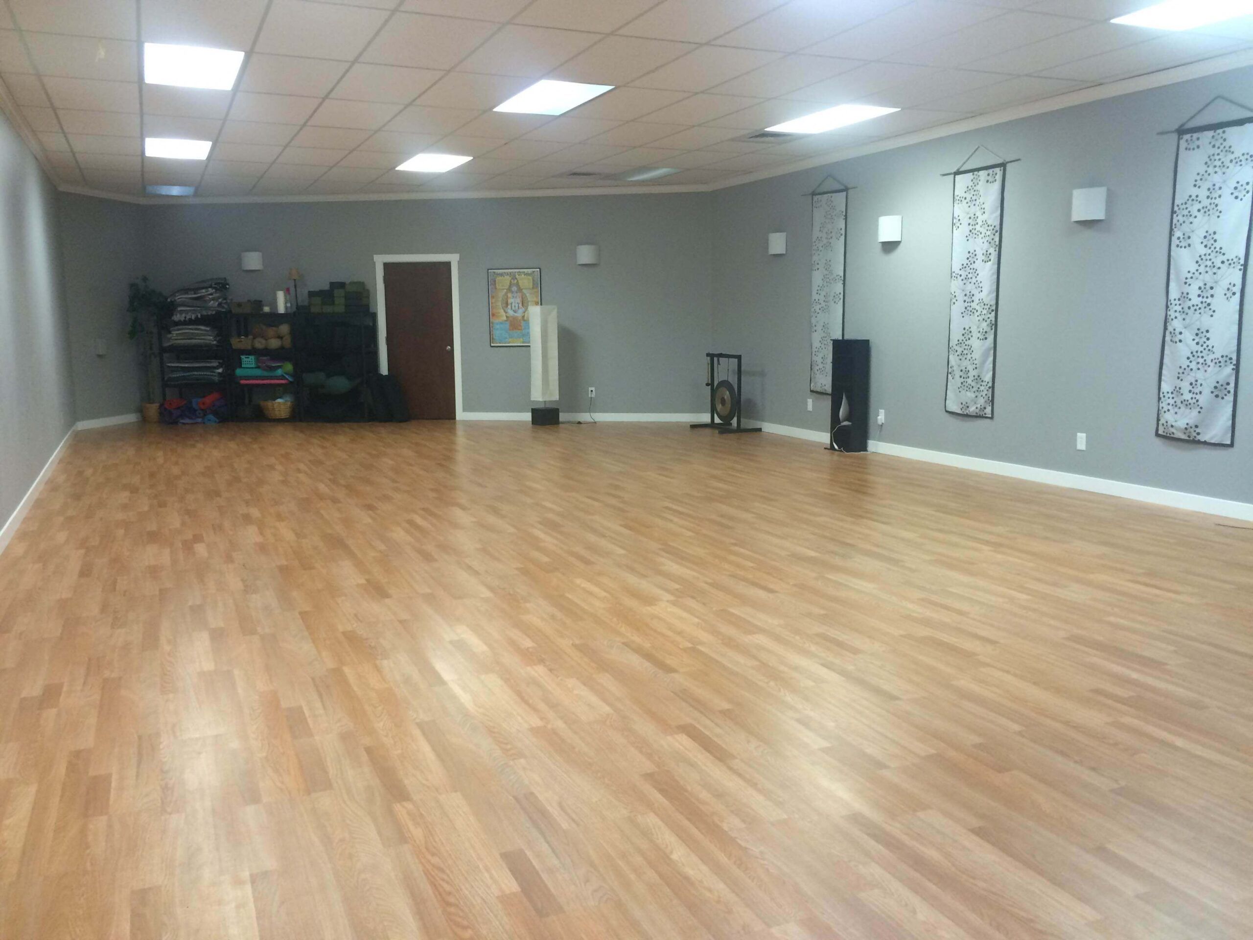 Spacious, empty room with eco-friendly wood flooring, yoga mats and props stacked in the corner, light gray walls, and three decorative wall hangings. Ceiling lights illuminate the funky space. Soul Flower Blog: Hippie Style & Kind Living