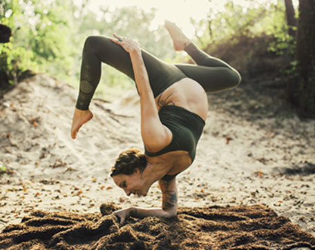 Person performing a challenging yoga pose balanced on one arm outdoors on a mat, surrounded by trees and natural light, wearing comfortable Boho Maternity Clothes that blend seamlessly with the serene, natural setting.